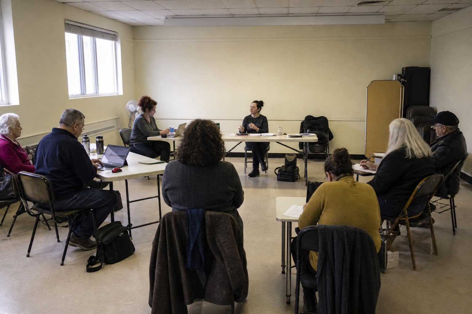 Illustration générée par IA : dans un local associatif modeste, un groupe varié suit à distance une formation sur l’évaluation d’un assistant numérique.