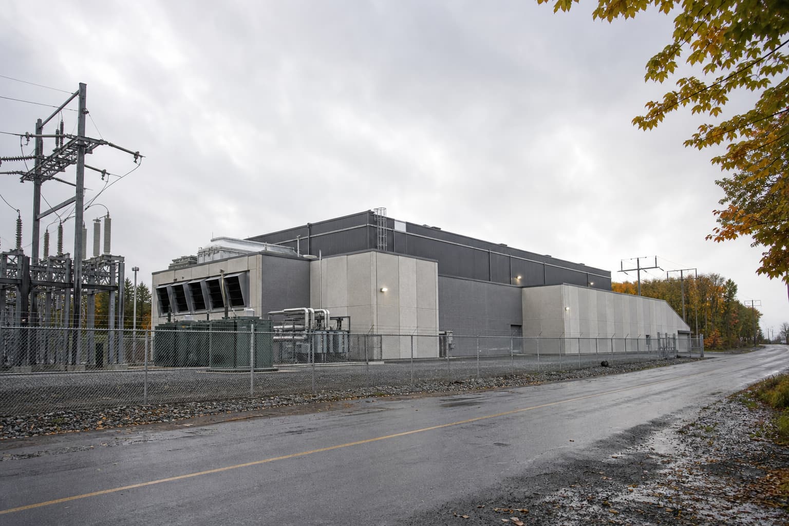 Illustration générée par IA : vue extérieure d’une infrastructure de données sobre près d’un poste électrique québécois, avec clôture et lignes de distribution.